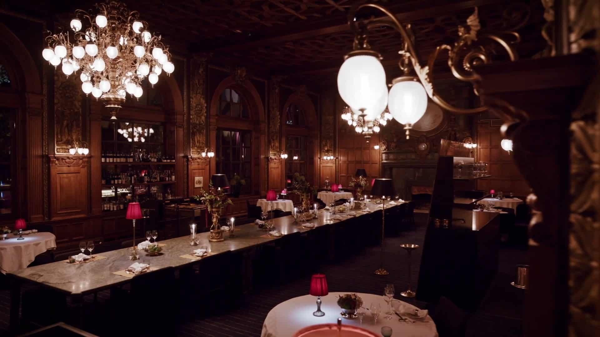 The dining room of Operakällaren: carved panelling, chandeliers and tables lit with red lamps