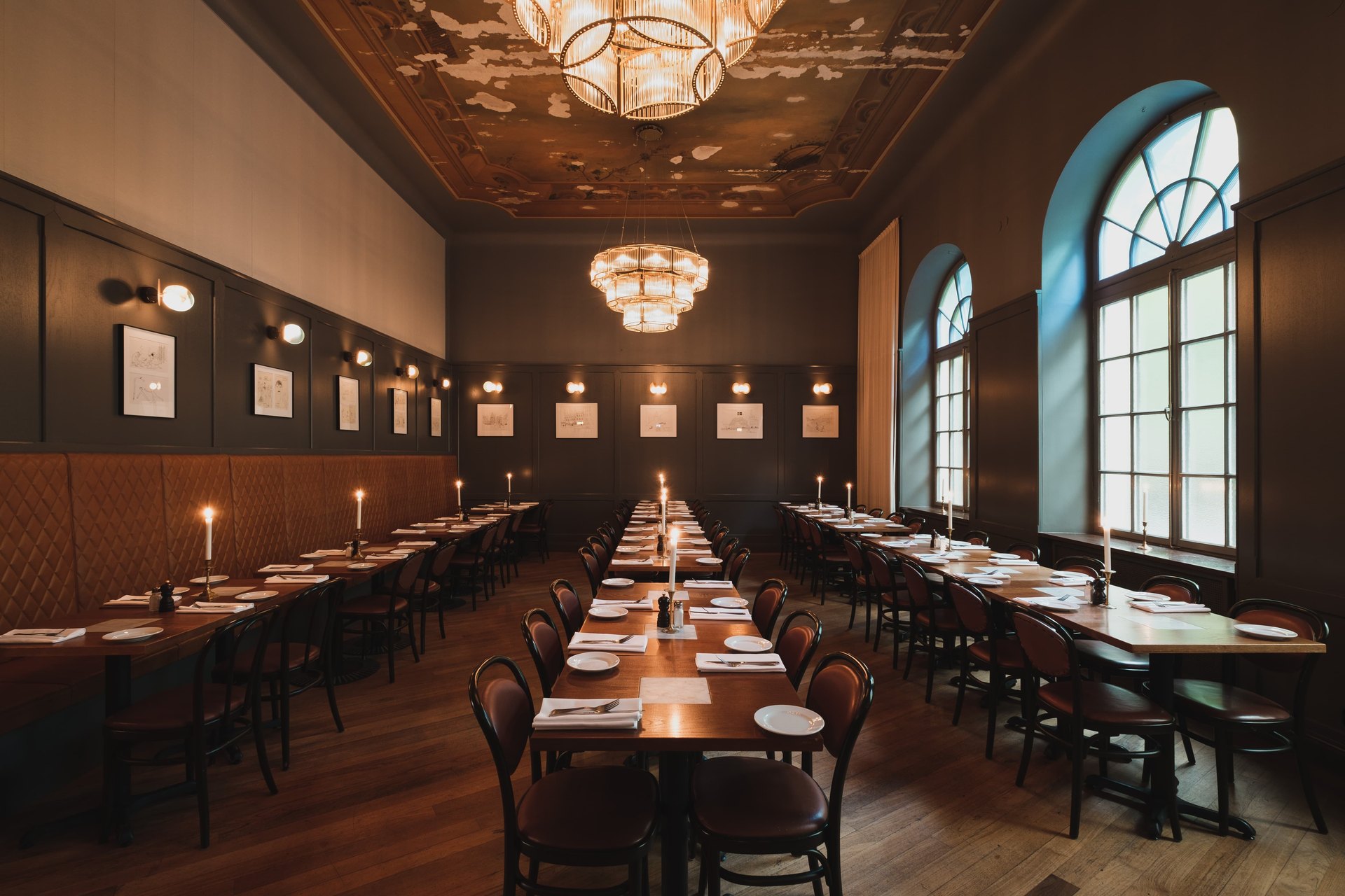 The long dining hall of Pelikan, with candles on the tables and arched windows